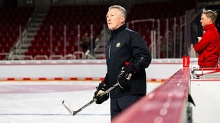 Eishockey-Nationaltrainer Harold Kreis hält einen Eishockey-Schläger in den Händen und steht auf dem Eis. 