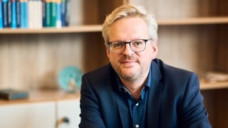 Ökonom Nils Goldschmidt lächelt in die Kamera.  Länder mit hohem sozialen Zusammenhalt sind wirtschaftlich erfolgreicher. Das Weltethos Institut Tübingen will das in konkrete Projekte umsetzen. In SWR1 Leute erläutert Ökonom Nils Goldschmidt die Projekte des Instituts.