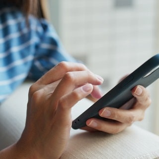 Zu sehen ist eine Frau, die mit ihrer Hand auf einem schwarzen Handy tippt.