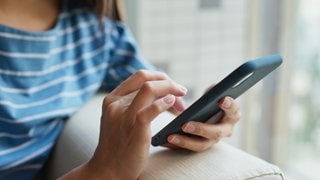 Zu sehen ist eine Frau, die mit ihrer Hand auf einem schwarzen Handy tippt.