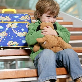 Kind mit kleinem Koffer sitzt auf einer Treppe und drückt sein Gesicht an einen Teddybär: Jedes Jahr werden in Deutschland Tausende Kinder vom Jugendamt in Obhut genommen. Ist das für die betroffene Familien wirklich eine Hilfe?