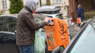 Symbolbild: Ein Mann holt eine Pfandflasche aus einem Mülleinmer.