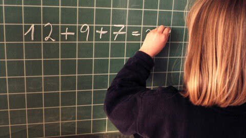 Mädchen schreibt mit linker hand an Tafel. Bis in das späte 20. Jahrhundert war es in Deutschland verbreitet, linkshändige Kinder "auf rechts" umzugewöhnen - Unterstützung für Linkshänder und ihre Besonderheiten fehlte.