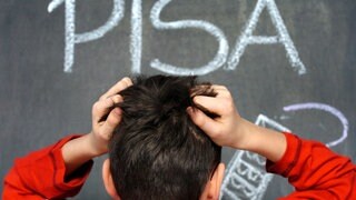 Ein Schüler rauft sich die Haare vor einer Kreidetafel, auf der das Wort PISA geschrieben steht.