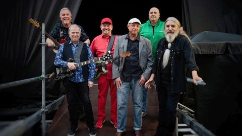 Die Spider Murphy gang steht am Bühnenaufgang in Kostüm und mit Instrumenten und sie schauen alle direkt in die Kamera.