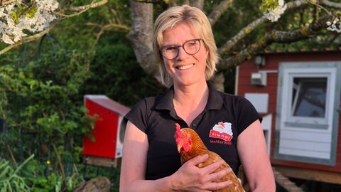 Simone Metzger ist mit einem Huhn, das sie bei sich aufgenommen hat, im Garten.