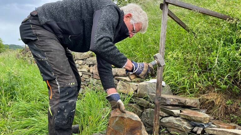 Kursleiter Günther Werner spaltet einen Stein für eine Trockenmauer.