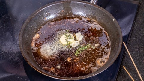 Zerlassene Butter in einer Pfanne mit Knoblauch und Thymian.