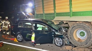 Ein Auto liegt verkeilt unter einem Traktoranhänger