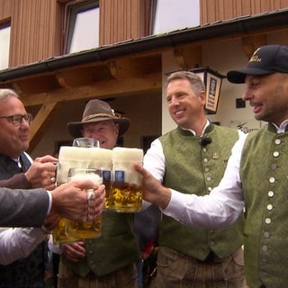 Das Wirtshaus in Aitrach wird wiedereröffnet. Männer stoßen mit Bierkrügen an.