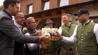 Das Wirtshaus in Aitrach wird wiedereröffnet. Männer stoßen mit Bierkrügen an.