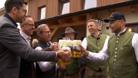 Das Wirtshaus in Aitrach wird wiedereröffnet. Männer stoßen mit Bierkrügen an.