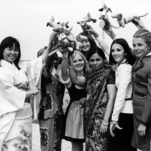 Bereits im April 1971 stellten sich die ersten Hostessen für die Olympischen Spiele 1972 in München vor. Die jungen Frauen aus Japan, Ghana, Indien und Brasilien präsentierten sich mit deutschen Kolleginnen auf dem Oberwiesenfeld und winkten mit dem Maskottchen der Spiele, dem Olympia-Dackel Waldi. 