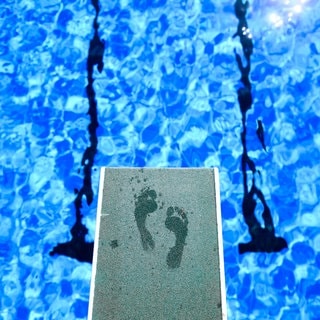 Symbolbild: Fußabdrücke eines Badegastes sind auf dem Ein-Meter-Brett im Freibad zu sehen.