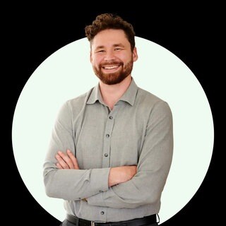 Paar- und Sexualtherapeut und Speaker Gavin Sexton steht mit verschränkten Armen vor einer schwarzen Wand mit weißem Kreis.