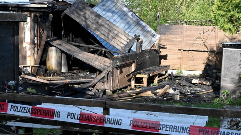 Absperrband vor einer zerstörten Gartenhütte. Das Dach der Hütte ist beim Brand in der Kleingartenanlage in Langenau eingestürtzt. 