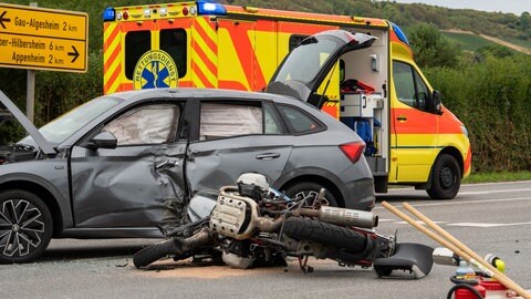 Ein Motorrad liegt zerstört vor einem zerbeulten Auto. Bei einem Unfall auf der L416 bei Gau-Algesheim ist ein Motorradfahrer schwer verletzt worden. 