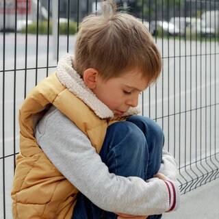 Porträt eines kleinen Jungen, der weint, während er alleine auf der Straße sitzt.