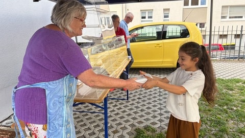 Eine Frau überreicht einem Mädchen eine Vesperbox mit einem gesunden Pausenbrot.