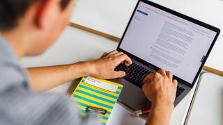 Ein Schüler eines Gymnasiums sitzt vor einem Laptop und benutzt ein KI-Tool.