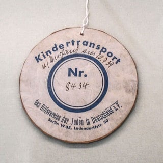 Anhänger an einem Teddybaer – Trostspender für eines der nach Großbritannien geretteten jüdischen Kinder, die 1938 und 1939 mit Kindertransporten verschickt worden waren. Bis 1939 kamen fast 10.000 Kinder nach Großbritannien. Viele sahen ihre Eltern nie wieder. – Exponat im Jüdischen Museum in Berlin. 