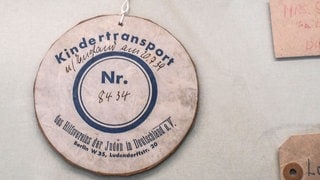 Anhänger an einem Teddybaer – Trostspender für eines der nach Großbritannien geretteten jüdischen Kinder, die 1938 und 1939 mit Kindertransporten verschickt worden waren. Bis 1939 kamen fast 10.000 Kinder nach Großbritannien. Viele sahen ihre Eltern nie wieder. – Exponat im Jüdischen Museum in Berlin. 