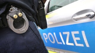 Ein Polizist mit Handschellen vor einem Polizeiauto: In Mainz wurde ein Mann wegen versuchten Mordes festgenommen, weil er Feuer in einer Wohnung gelegt haben soll. 