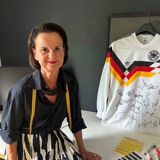 Trikot-Designerin Ina Franzmann sitzt neben einem Deutschland-Trikot mit Unterschriften.