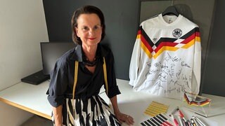 Trikot-Designerin Ina Franzmann sitzt neben einem Deutschland-Trikot mit Unterschriften.