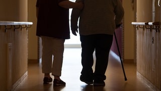 Eine Altenpflegerin stützt eine Heimbewohnerin beim Gehen