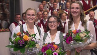 Drei junge Frauen halten Blumensträuße in der Hand und lächeln. Es sind die Kanditatinnen zur Wahl der Tettnanger Hopfenkönigin.