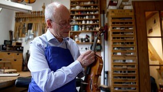 Der Geigenbaumeister Ralf Schumann hat eine Nadel in der Hand. Damit sticht er in das Griffbrett der Geige. 