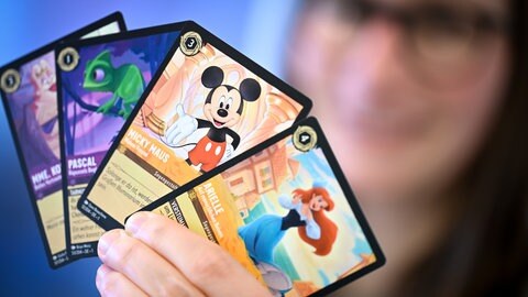 Eine Person hält Karten von Disney Lorcana, dem Sammelkartenspiel von Ravensburger, in den Händen.