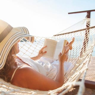Frau liegt in einer Hängematte und liest ein Buch