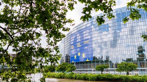 Der Himmel spiegelt sich in der gläsernen Fassade des Europäischen Parlaments in Straßburg. Ein großes Banner wirbt für die Europawahl.