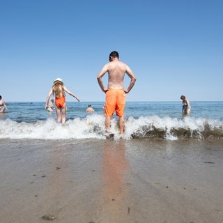 Menschen stehen im Wasser am Ostseestrand in Kühlungsborn.