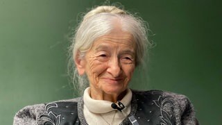 Alte Frau mit weißen Haaren lächtelt in Kamera.