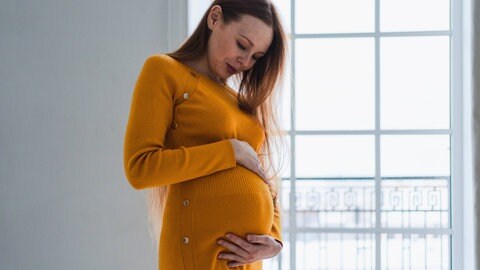 Eine schwangere Frau hält sich den Bauch.