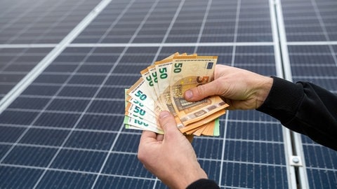 Mann hält Geldscheine in der Hand, Solaranlage im Hintergrund