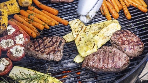 Tipps und Rezepte fürs Grillen: Gemüse wie Karotten, Tomaten und Zucchini sowie Steaks liegen auf einem Kugelgrill.