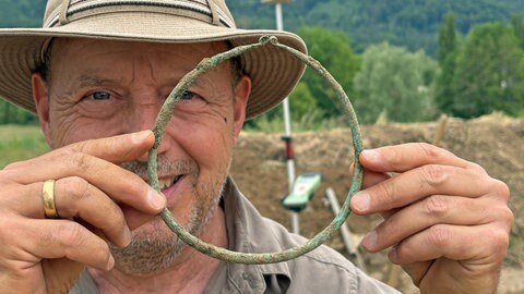 Ein Mann hält einen handtellergroßen Ring aus Bronze.