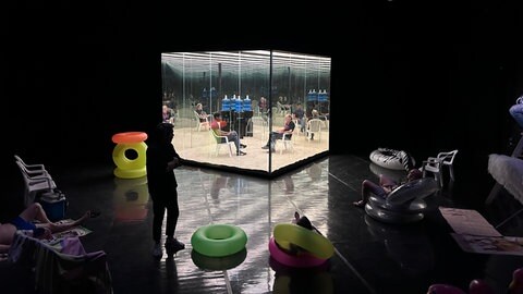 Ein Glaskasten im dunklen Theaterraum.