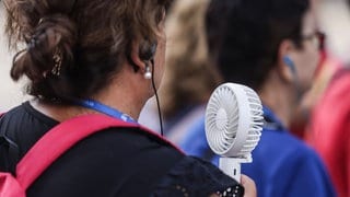 Weiter heiß: Eine Frau hält sich bei heißem Sommerwetter einen Handventilator vor das Gesicht.