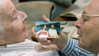 Ein älteres Paar betrachtet ein altes Urlaubsfoto: Ein Urlaub, bei dem die Stimmung anfangs mies war und dann immer besser wurde, wird rückblickend besser bewertet als einer, bei dem es genau andersherum war. Dieses Ende ist für die Bewertung der Erinnerung sogar noch wichtiger als die Peaks.