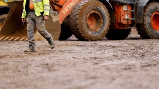 Ein Bagger und ein Arbeiter auf einer Baustelle (Symbolbild). Um Vorratsflächen für Unternehmen anbieten zu können, wollen alle Regionen der Westpfalz jetzt zusammenarbeiten.