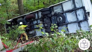 Bei Beilstein ist ein Wohn·mobil 15 Meter in die Tiefe gestürzt. Das Wohn·mobil liegt auf der Seite. Daneben steht ein Feuerwehr·mann. Rechts das SWR Logo für Leichte Sprache.