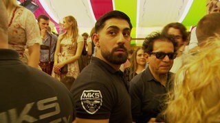 Ein Mitarbeiter der Security steht in einem Bierzelt auf dem Cannstatter Frühlingsfest. Er ist von einer Menschenmenge umgeben.