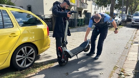 Ein Polizist kontrolliert im Rahmen der E-Scooter-Kontrollwoche den Roller eines Mannes in Mainz