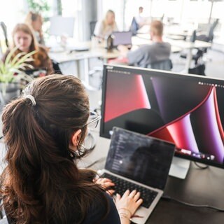 Auch in RLP tobt eine Debatte um den CDU-Vorschlag zur Teilzeit - In einem Großraumbüro arbeitet eine Frau an Laptop und Monitor (Symbol) 