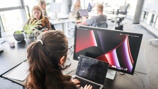 Auch in RLP tobt eine Debatte um den CDU-Vorschlag zur Teilzeit - In einem Großraumbüro arbeitet eine Frau an Laptop und Monitor (Symbol) 